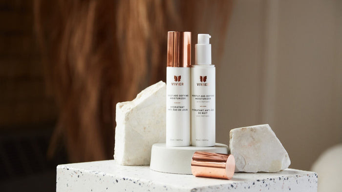 Vivier Daily Age-Defying Moisturizer and Nightly Age-Defying Moisturizer displayed on stone pedestals with rose gold caps.