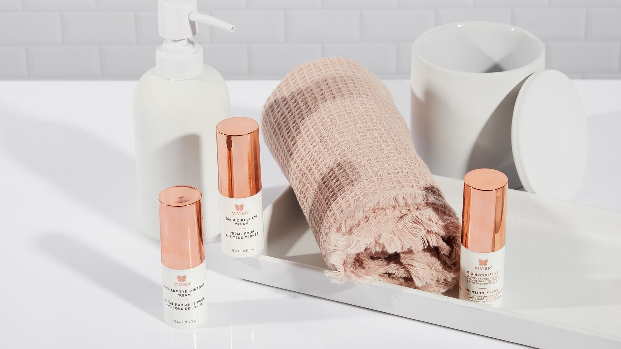 Three Vivier eye care products displayed on a bathroom countertop with a towel, soap dispenser, and mug.